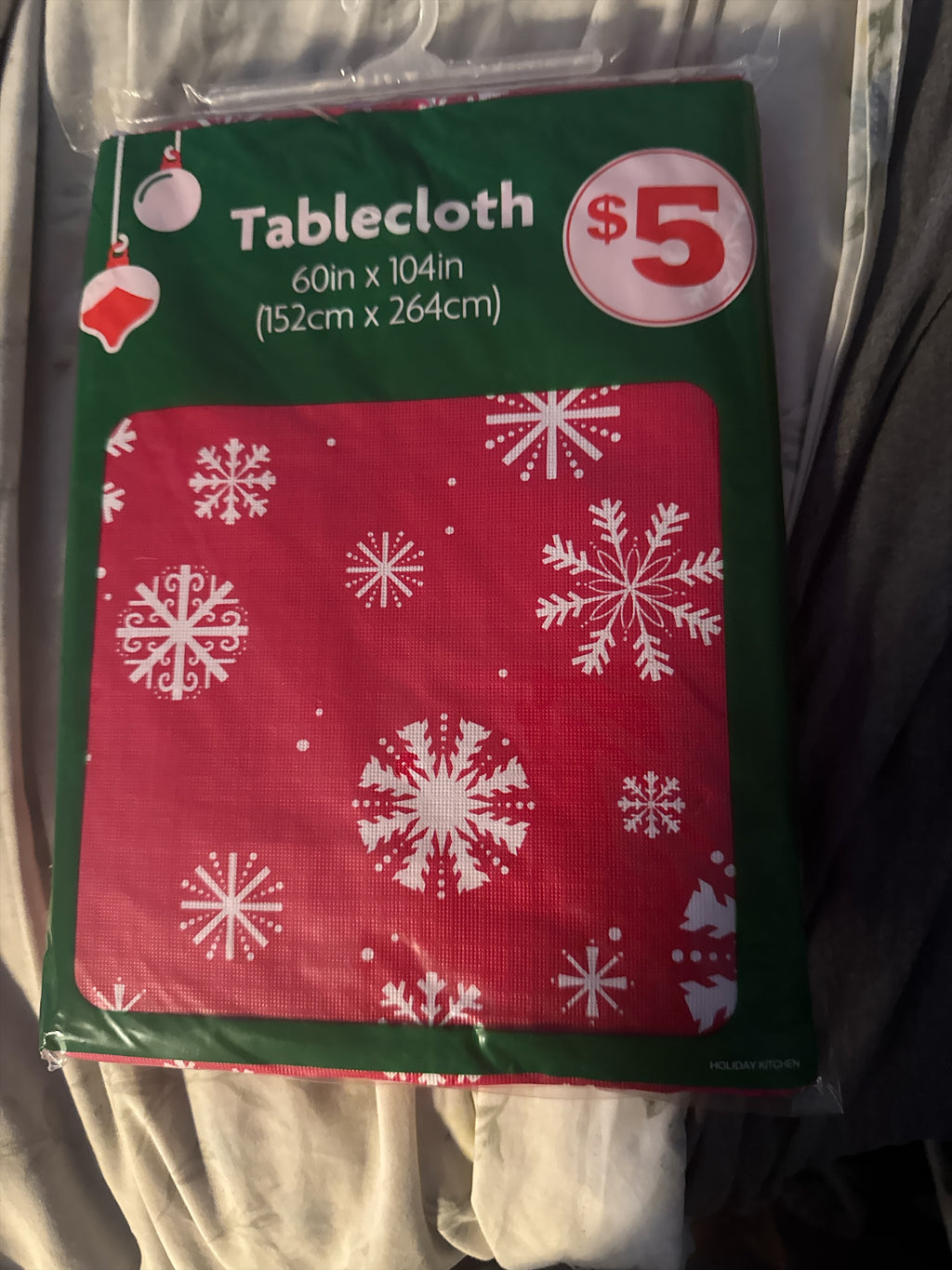The Flip Side rectangular holiday tablecloth in red with white snowflake patterns, 60 by 104 inches in packaging.