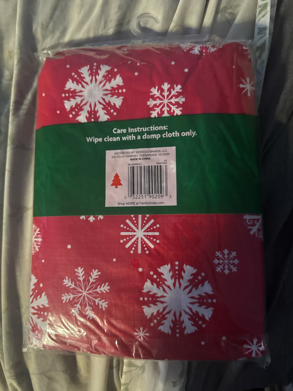 The Flip Side rectangular holiday tablecloth in red with white snowflake patterns, packaged in clear plastic.