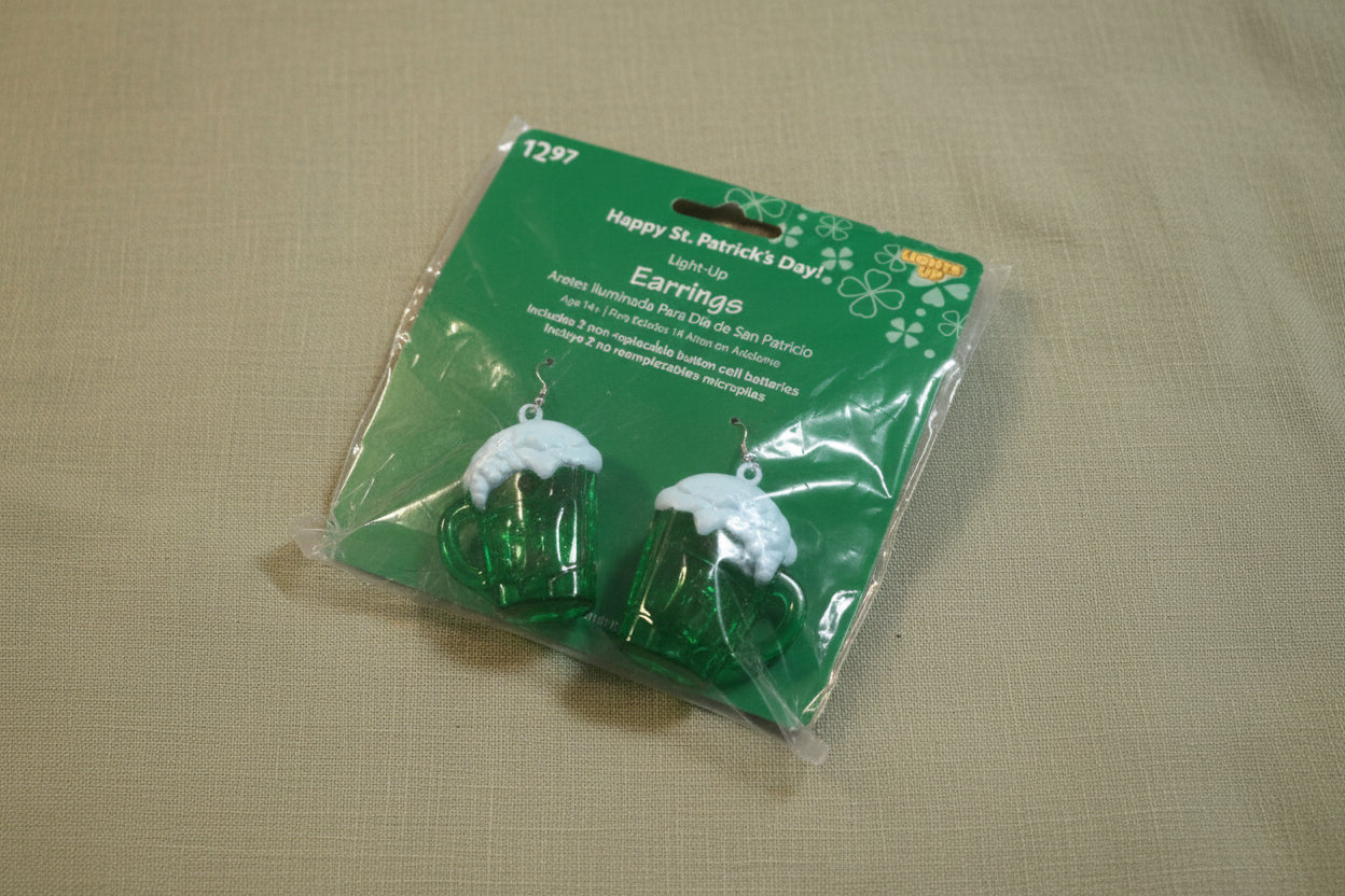 The Flip Side St. Patrick's Day light-up beer mug earrings in green with white foam detail in original packaging.